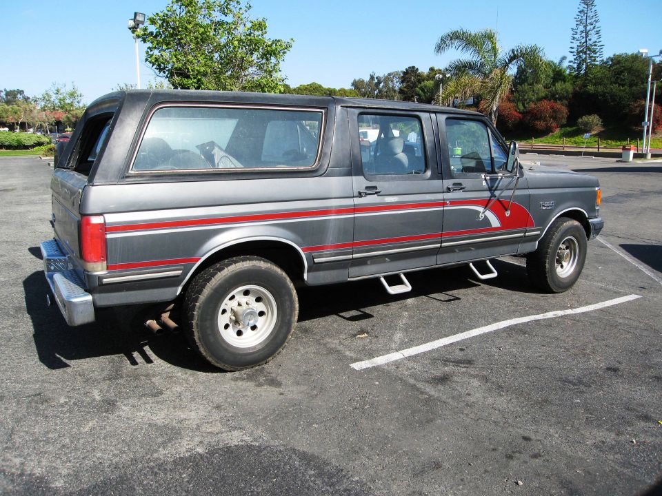 Gray Ford Bronco with red stripe and extended cab, parked in a lot