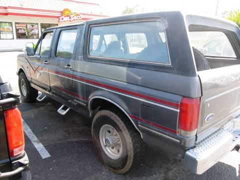 1986 Ford Bronco - This dark gray SUV, likely a 1987 Ford Bronco, is seen from the side with distinctive red and gray pinstripes.