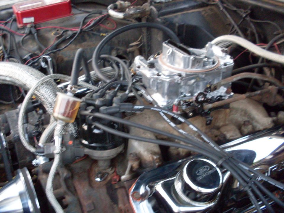 V8 engine bay with aluminum 4-barrel carb, braided lines, and chrome Ford valve cover