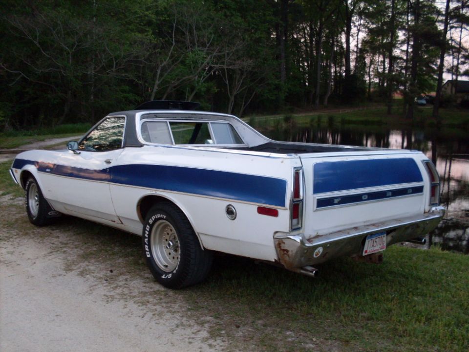 White Ford Ranchero with blue stripes, rear 3/4 view, parked by a pond