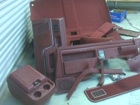 1989 Ford Bronco - Collection of maroon interior car parts laid out on a floor.