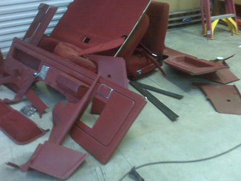 1989 Ford Bronco - Various red interior car parts, including door panels and seat sections, are disassembled and laid out on a floor.