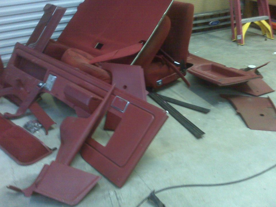 Pile of red car interior panels and seats on a concrete floor