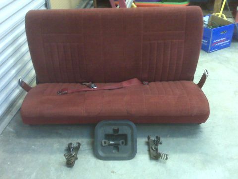 1989 Ford Bronco - Red bench seat with seatbelts and associated mounting hardware displayed on a concrete floor.