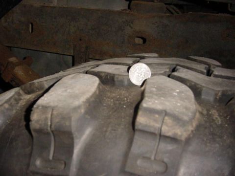 1992 Ford Bronco - Close-up of a large mud-terrain tire's aggressive lug tread with a US quarter stood on edge between the blocks to show tread depth, the coi…
