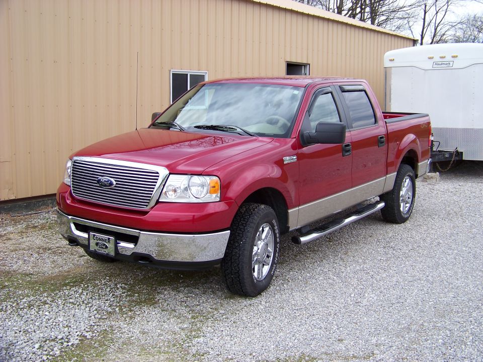 Red pickup truck with tan lower body panels and chrome accents, parked on gravel. A white trailer is attached