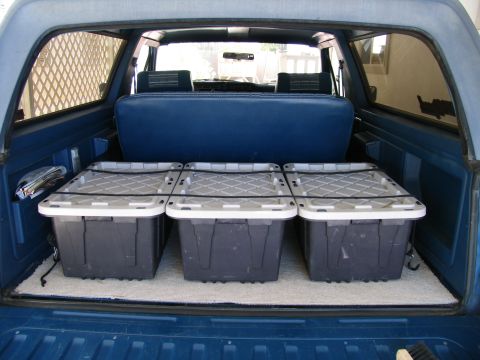 1984 Ford Bronco - Blue-interior SUV cargo area loaded with six black lidded plastic storage bins arranged in two rows of three.