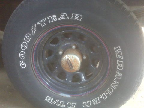 1995 Ford Bronco - A close-up view of a tire and wheel assembly, showing brand markings and a rusty hub.