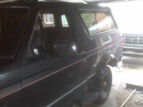 1995 Ford Bronco - The side profile of a black Ford Bronco is visible, with a second vehicle parked behind it.