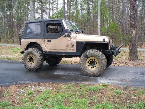 1992 Ford Mustang - This tan Jeep Wrangler features a black soft top and aggressive off-road tires with distinctive yellow accents on the wheels.
