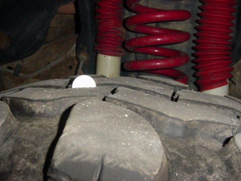 1992 Ford Bronco - A coin is placed on the tread of a large off-road tire, with red suspension components in the background.