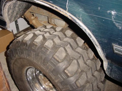 1992 Ford Bronco - Close-up of a chunky aggressive-lug mud-terrain tire on a chrome wheel stuffed into the front wheel well of a dark teal truck, shot inside…