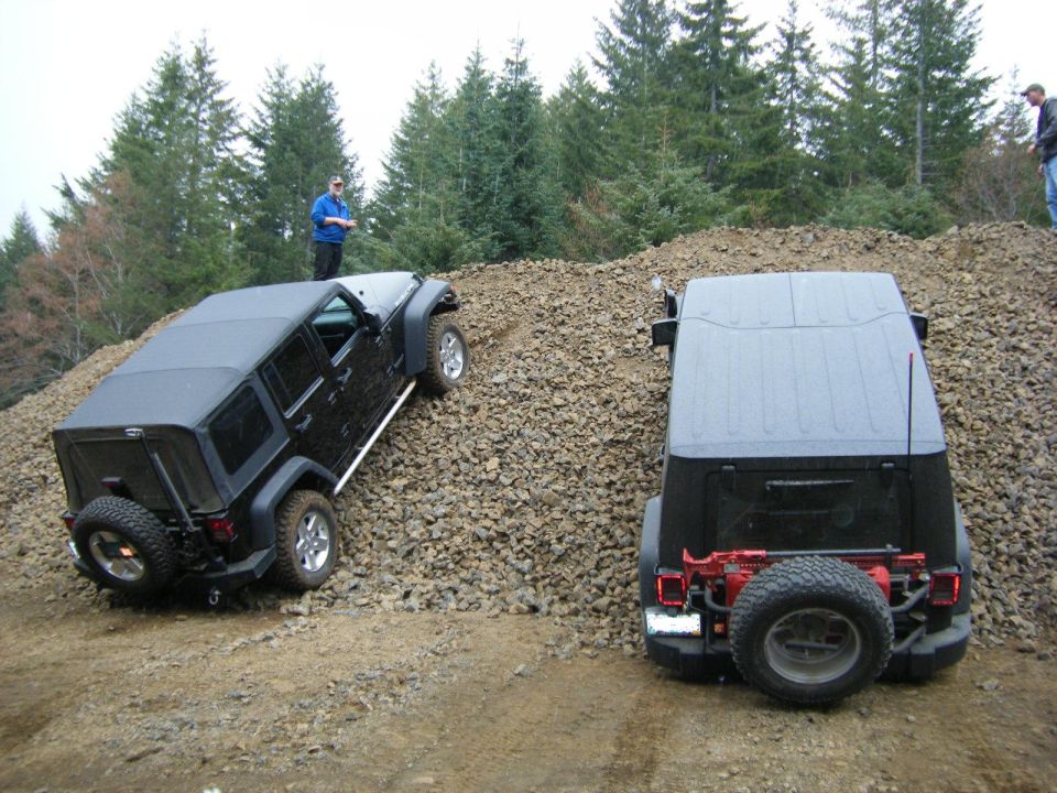 Two black Jeep Wranglers on a rocky hill with a forest behind them.