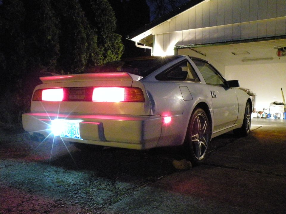 Silver Nissan 300ZX rear view at night, parked in driveway with illuminated taillights and license plate.
