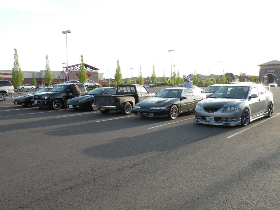 Several cars parked in a lot, including a silver sedan, black coupe, black pickup truck, and black SUV.