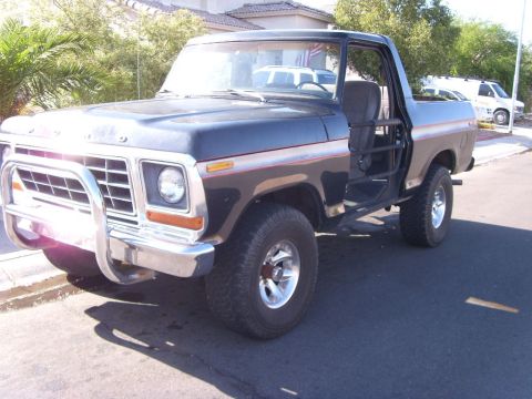 1978 Ford Bronco - Black and silver two-tone full-size Ford Bronco parked at a suburban curb with the top and doors off, showing tube door bars, a gray cloth…