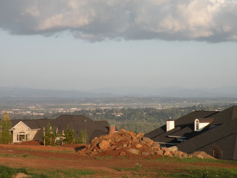 Houses under construction on a hillside overlooking a city and mountains.