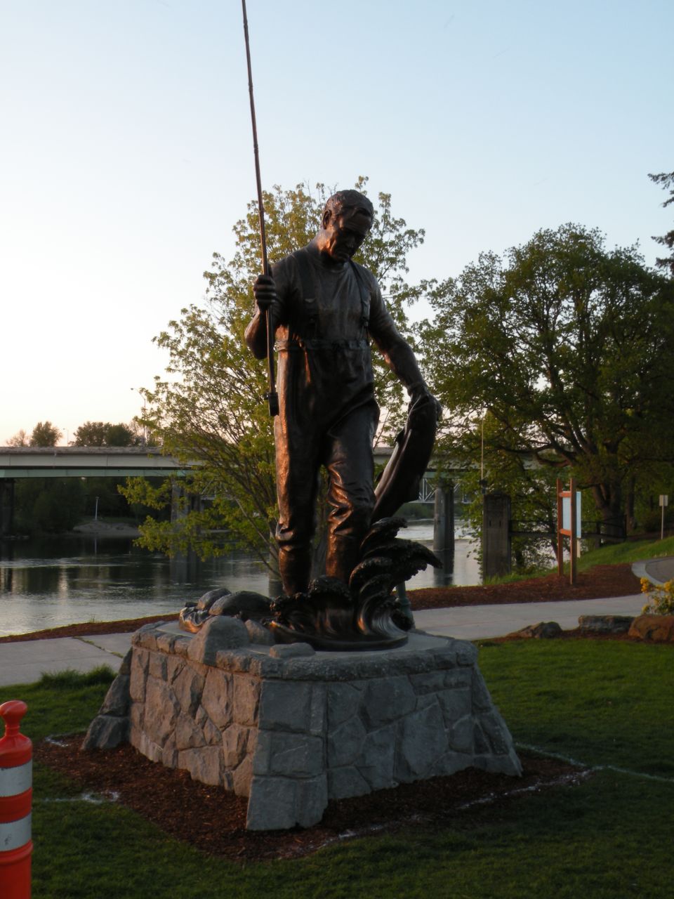 Statue of a fisherman holding a fish and fishing pole by a river.
