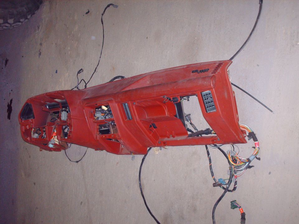 Red dash panel with wiring harness lying on a concrete floor