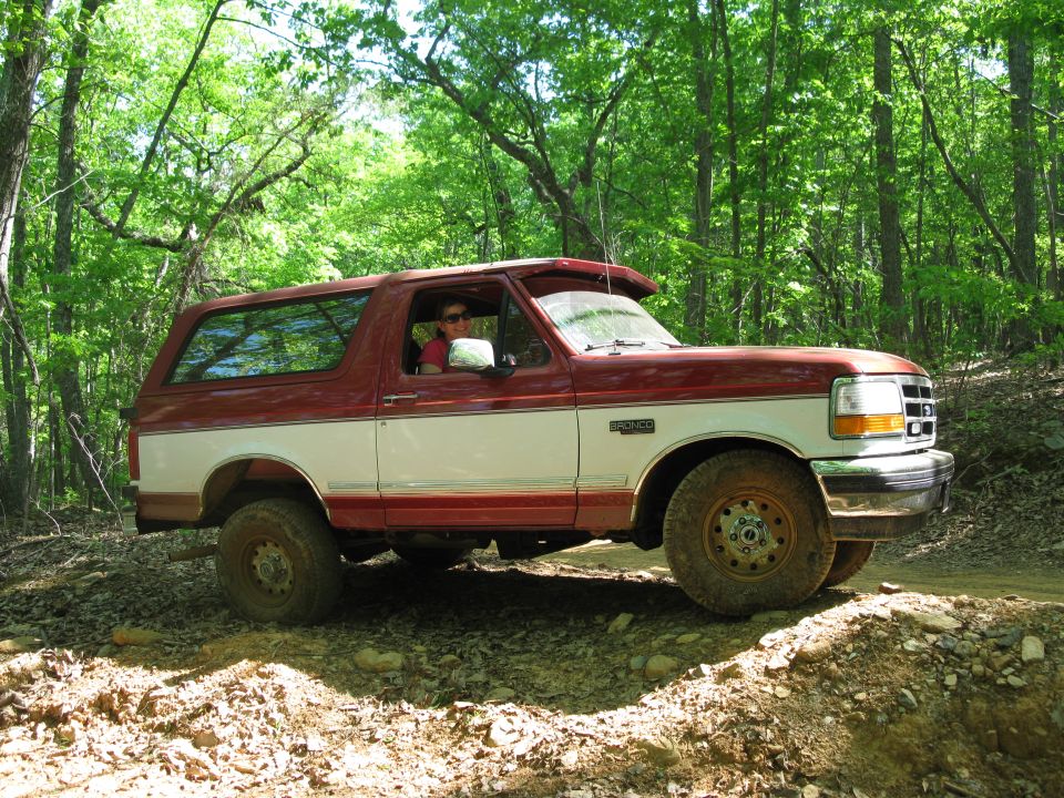 Red and white Ford Bronco driving on a dirt trail in the woods