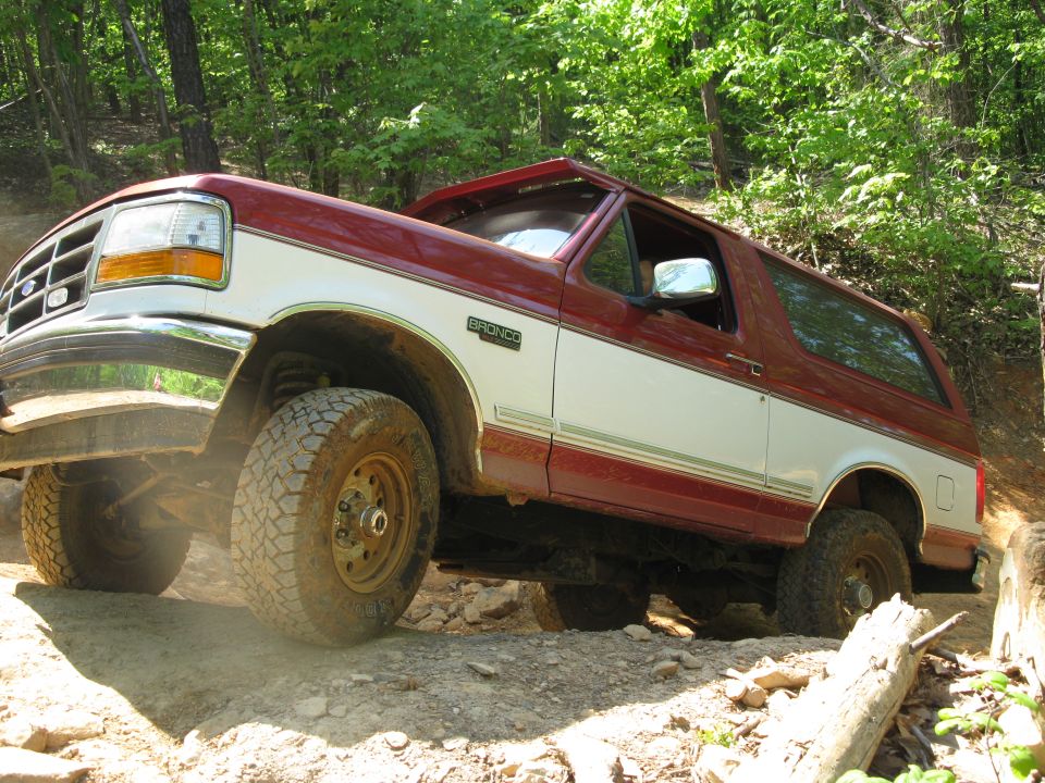 1995 Ford Bronco climbing a rocky hill, red and white paint, off-road tires