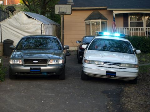 1999 Ford Crown Victoria - Two Ford Crown Victoria sedans are parked in front of a house, one appears to be a police car.