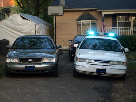 1999 Ford Crown Victoria - Two Ford Crown Victorias are parked in a driveway, one a white police car with its emergency lights activated.