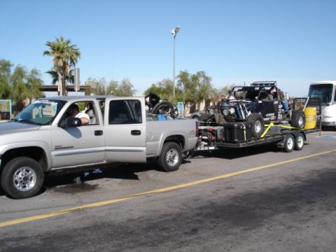 2008 Ford Bronco - A silver four-door pickup truck is towing a trailer with a black off-road buggy. The truck has a driver and passenger visible in the cab.