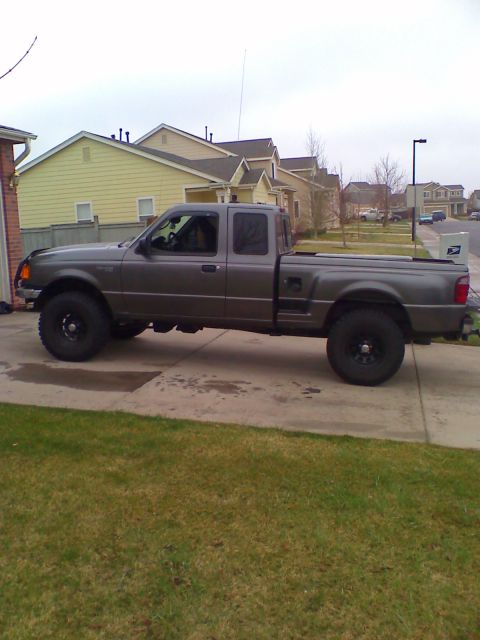 2004 Ford Ranger - A side view of a dark gray Ford Ranger pickup truck parked on a concrete driveway in front of a row of houses.