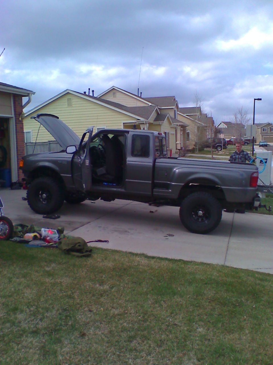 Gray four-door Ford Ranger pickup truck with hood and driver's door open in a driveway.