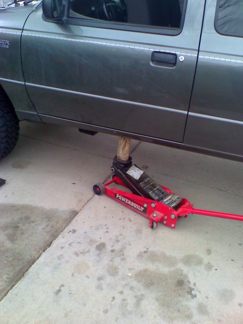 2004 Ford Ranger - A red Powerbuilt hydraulic floor jack is supporting the frame of a gray Ford Ranger pickup truck. The truck is lifted off the ground, and t…