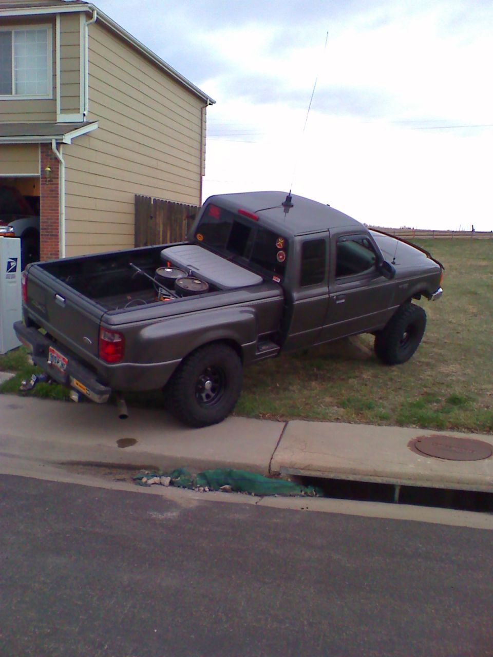 Gray lifted Ford Ranger extended-cab pickup parked at curb, rear 3/4 view