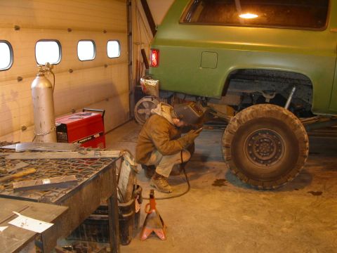 1990 Chevrolet Suburban - A person wearing a welding mask and protective clothing is welding underneath the rear quarter panel of a green Chevrolet Suburban. A large…