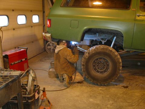 1990 Chevrolet Suburban - A person in protective gear is welding underneath a green Chevrolet Suburban in a garage. A red welding machine is visible to the left of t…