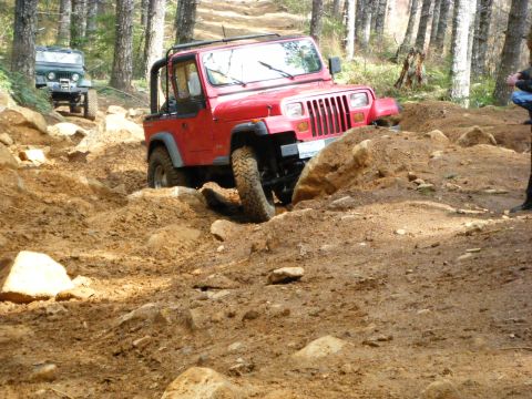 2005 Jeep Wrangler - A red Jeep Wrangler is navigating a steep, muddy, and rocky off-road trail. Another green Jeep is visible further up the trail.