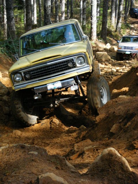 2005 Jeep Wrangler - A yellow Jeep CJ is navigating a steep, rocky, and muddy off-road trail in a forest. The vehicle is angled sharply to the right as its fron…