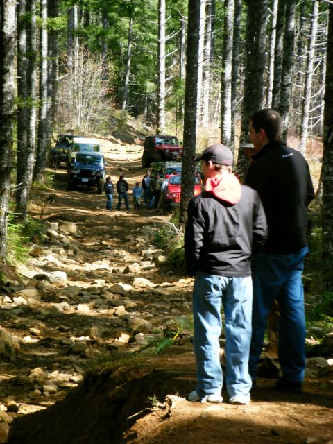2005 Jeep Wrangler - A group of people and several Jeep Wranglers are gathered on a rocky, wooded trail. The Jeeps appear to be in various stages of off-road dr…