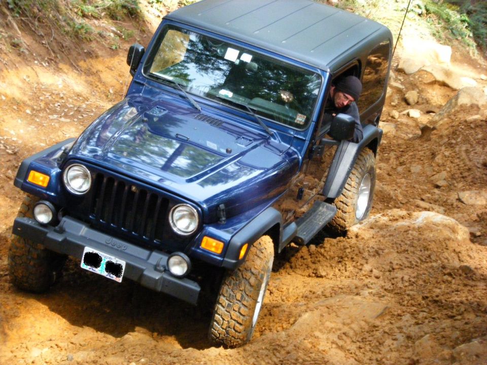 Blue Jeep Wrangler off-roading on a muddy, rocky trail.