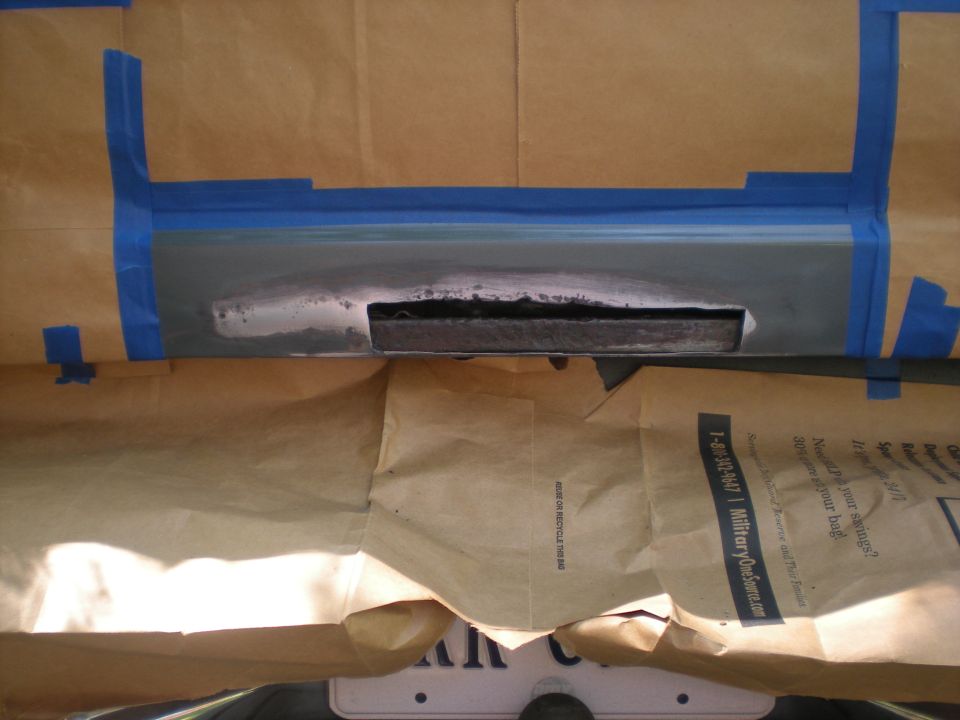 Vehicle body panel masked with tape and paper, showing a cutout.