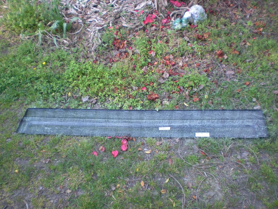 Dark gray textured trim piece on the ground with grass and leaves