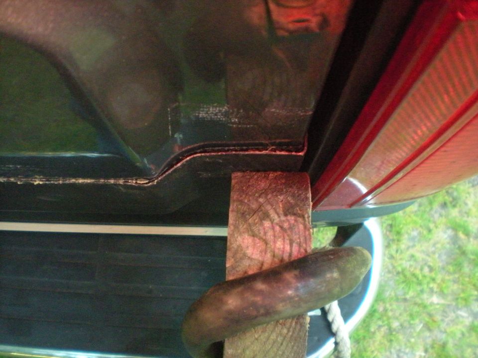 Underside of dark vehicle body panel with wood block and rope, red taillight visible.