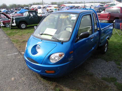 2001 Ford Crown Victoria - A blue three-wheeled microtruck is displayed at an outdoor event with other vehicles in the background.