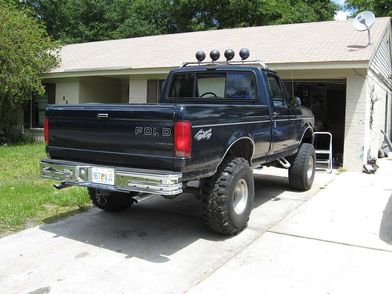 Black 1993 Ford F-150 pickup truck with lifted suspension and off-road tires, viewed from the rear