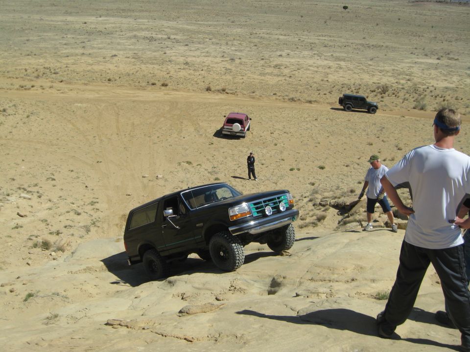 Black Ford Bronco climbing rocky terrain, green grille, auxiliary lights