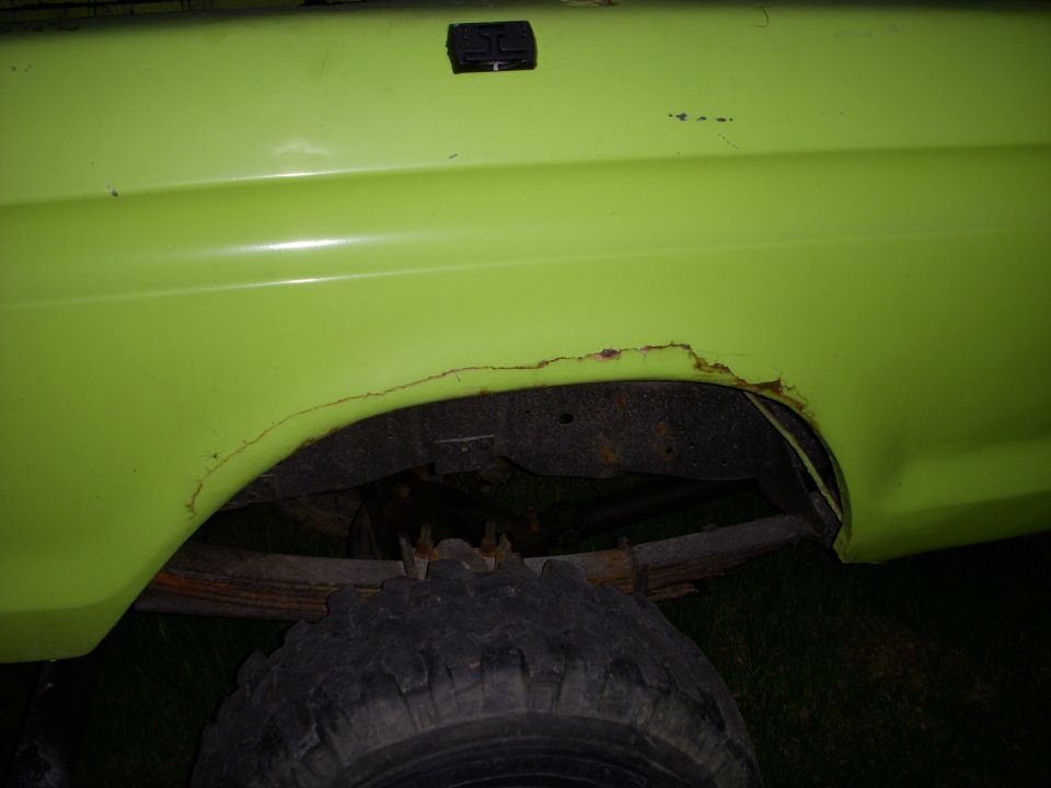 Rust damage and torn wheel arch lip on lime green pickup fender above mud tire