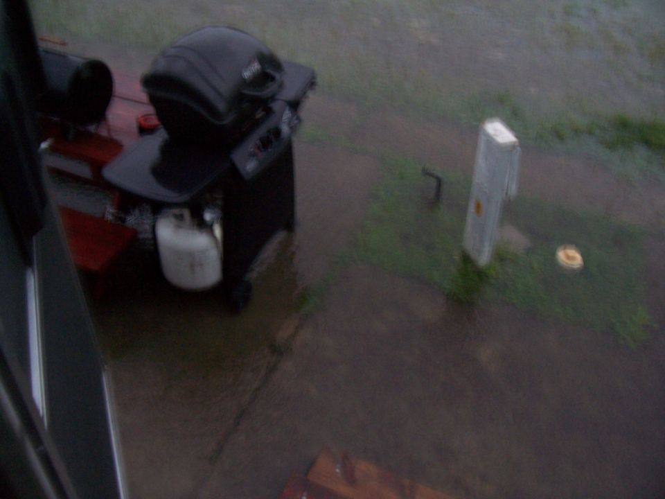Gas grill with propane tank on a wet patio during rainfall