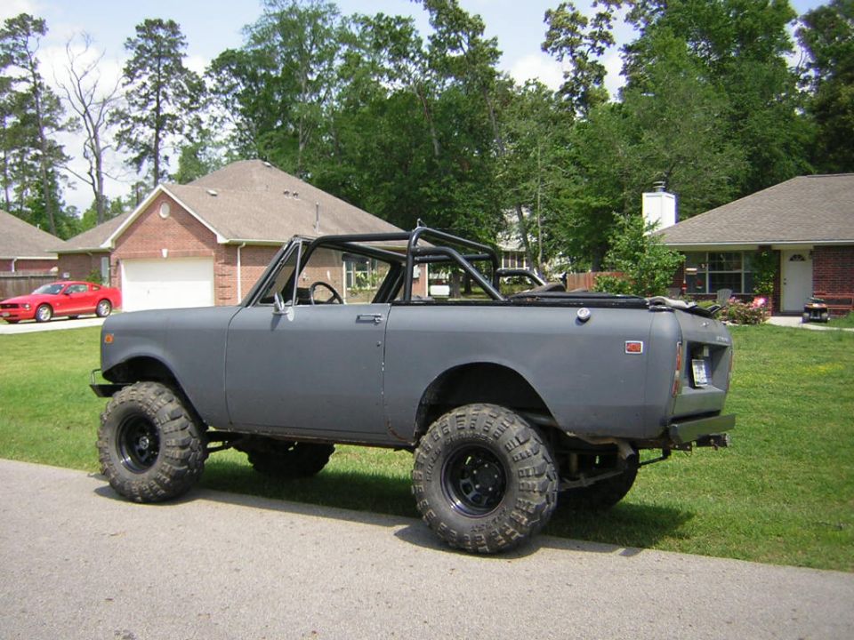 Gray primered topless International Scout II with roll bar, lifted on mud tires, side view
