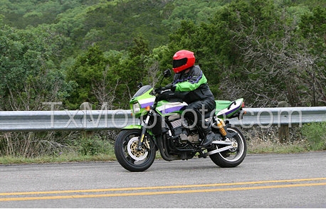 1981 Kawasaki Bayou - A motorcycle rider travels down a road with trees and a guardrail in the background.