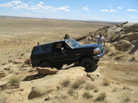 1993 Ford Bronco - A black Ford Bronco navigates rocky terrain under a partly cloudy sky.