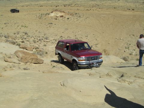 1993 Ford Bronco - A red and white Ford Bronco navigates a desert off-road trail, with another vehicle visible in the distance.